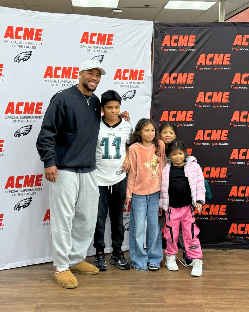 Students pose for photo with Saquon Barkley in front of ACME backdrop.