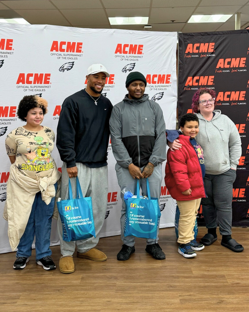 Family poses for photo with Saquon Barkley in front of ACME backdrop.