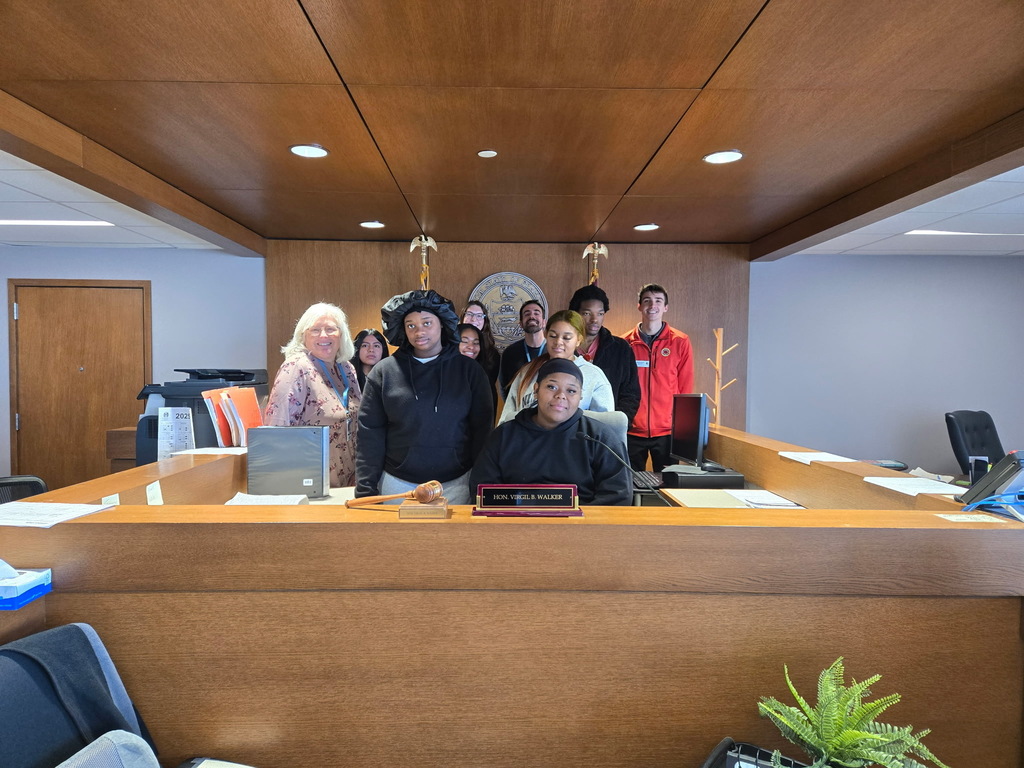 Students and a teacher are behind the judge's desk while on a field trip to the courthouse