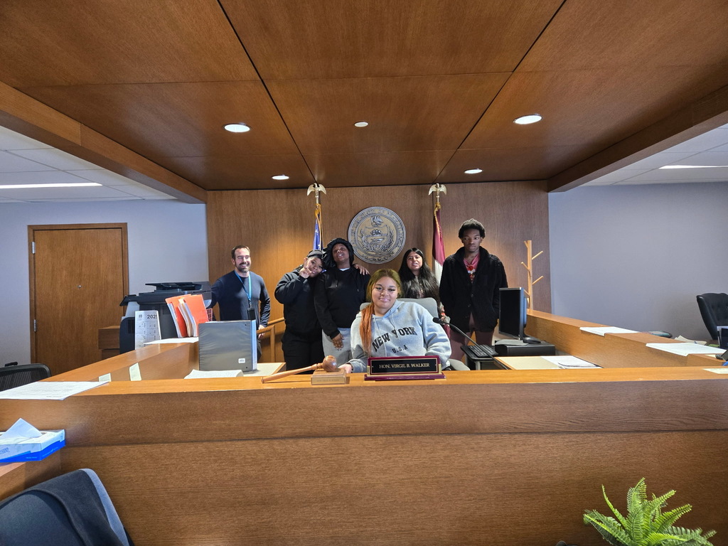Students and a teacher are behind the judge's desk while on a field trip to the courthouse