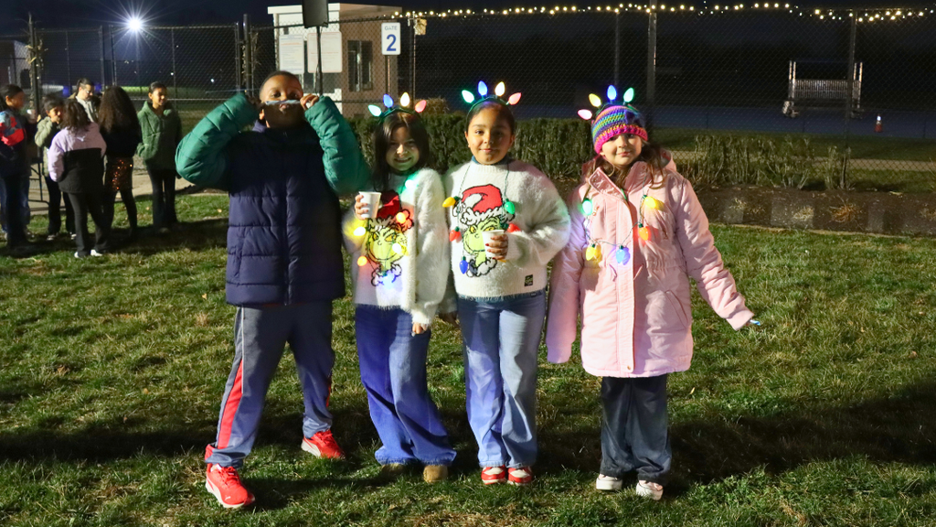 Four students holding hot chocolate cups and candy canes ready to sing.