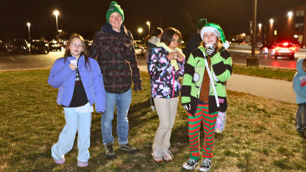 Students and parent pose for a photo holding hot chocolate cups. 