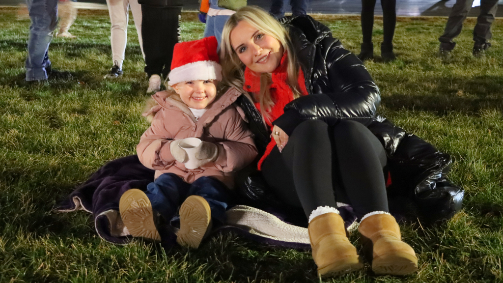 Parent and student smile for a photo while sitting on a blanket for the Very Merry Sing Along. 