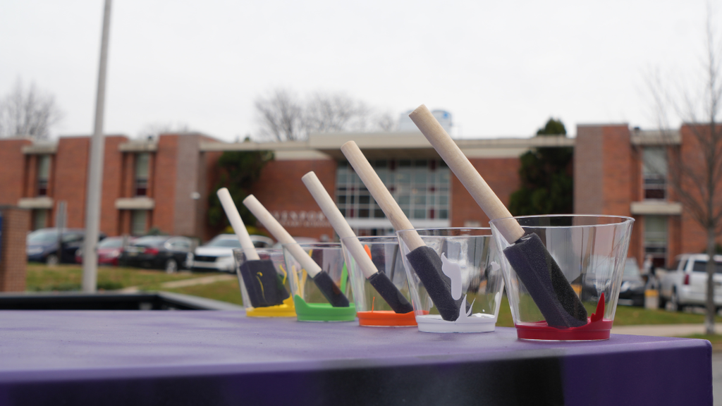 Cups of paint and foam brushes lined up on table ready for students to use.