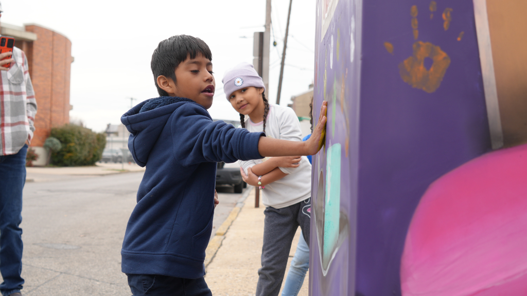 One student watching another student put their handprint on the box.