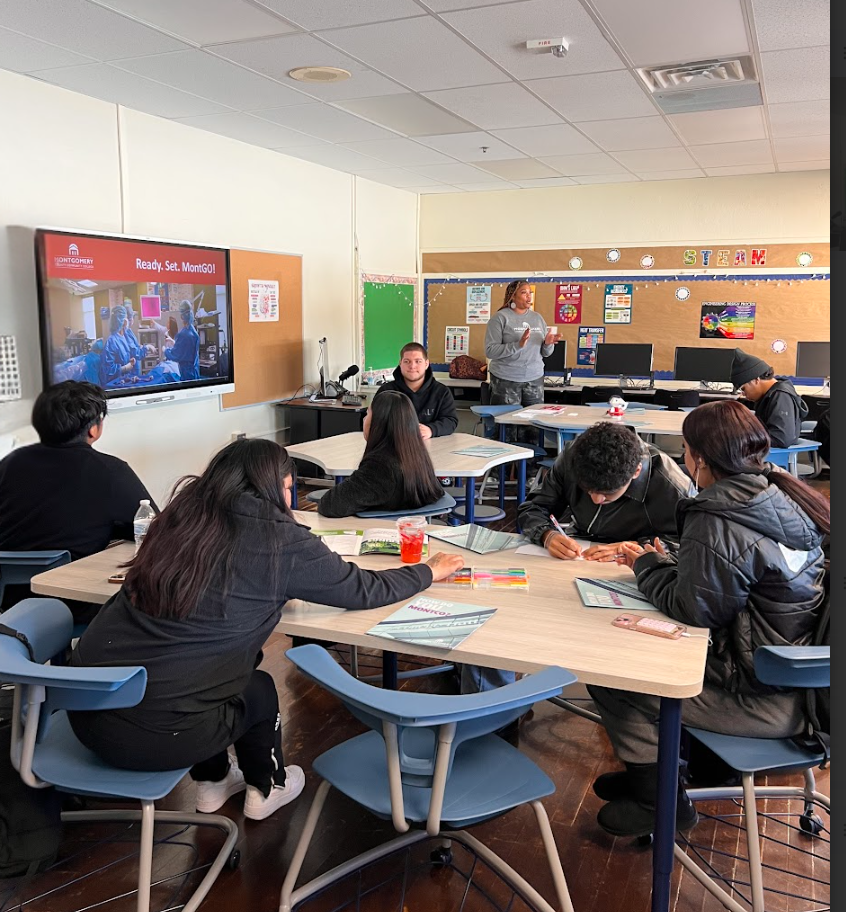Students are sitting in a classroom listening to a speaker and filling out a paper.