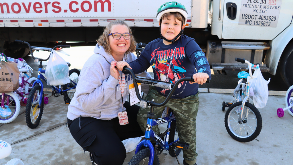 Teacher kneels next to student on bicycle wearing a helmet. 