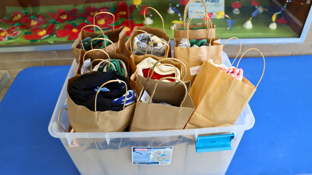 Plastic bin with gift bags that have sets of pajamas. 
