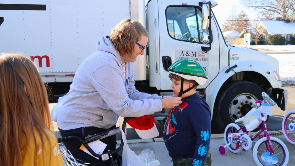 Teacher helps a student buckle his helmet before riding his new bike. 
