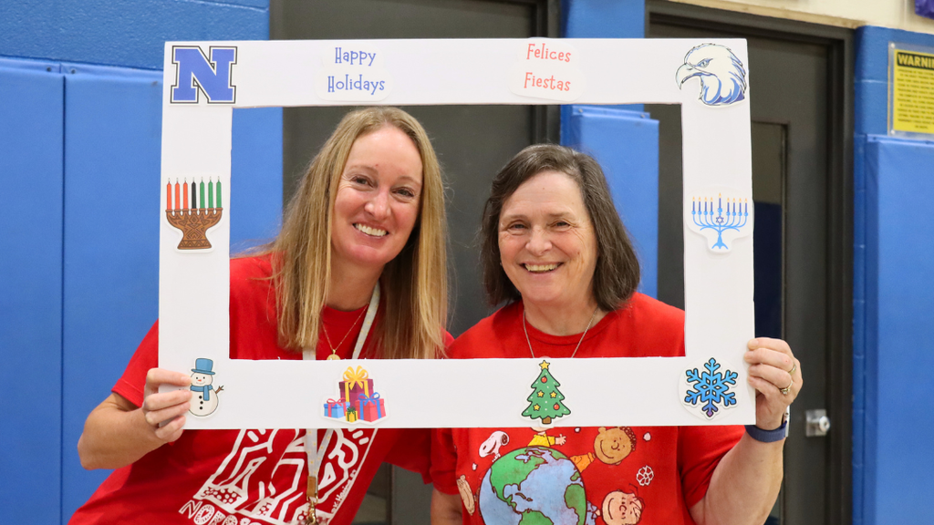 Two staff members holding a poster frame with text "Happy Holidays" and holiday decorations.