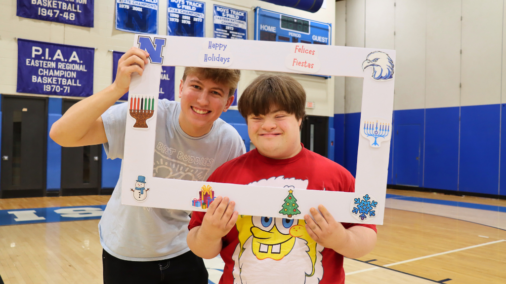 Two students holding a poster frame with text "Happy Holidays" and holiday decorations.