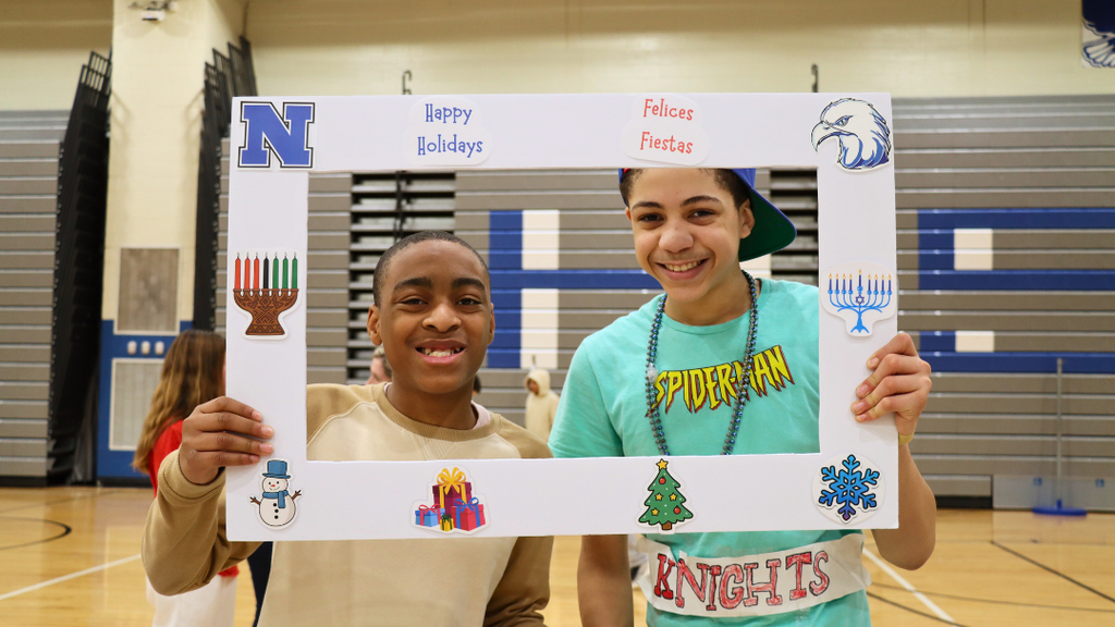 Two students holding a poster frame with text "Happy Holidays" and holiday decorations.