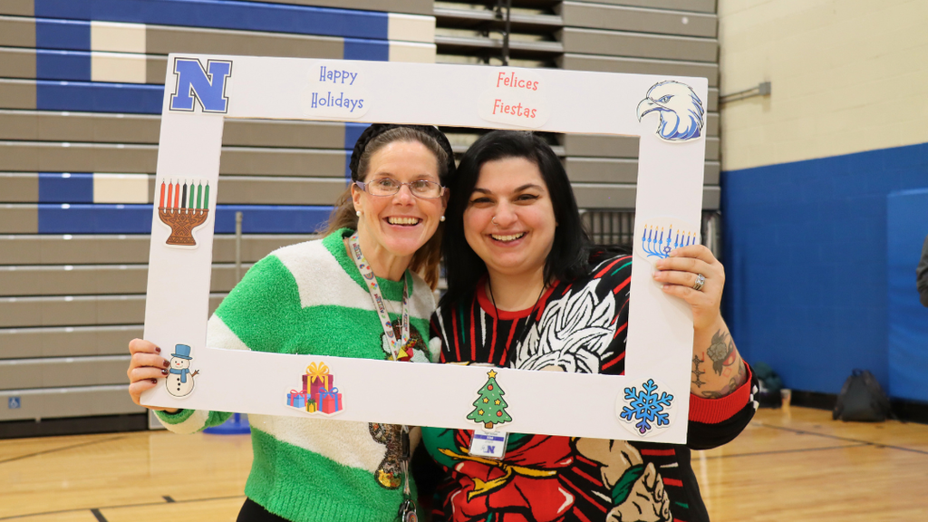 Two staff members holding a poster frame with text "Happy Holidays" and holiday decorations.