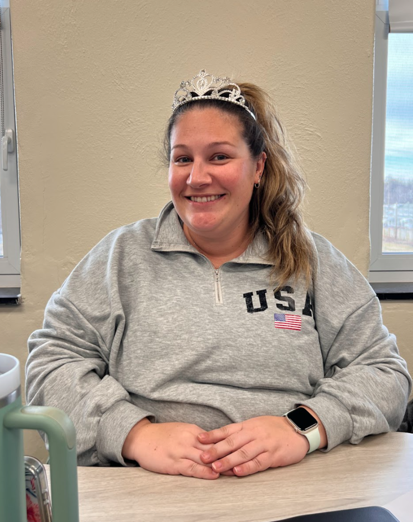 Photo of a teacher wearing a crown at a desk.