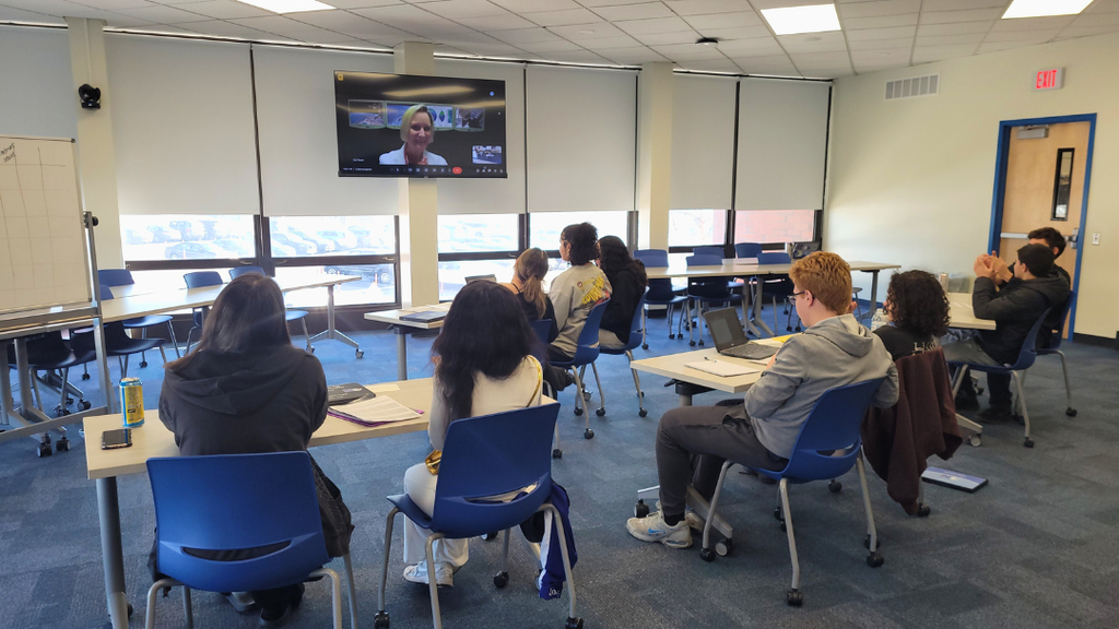 Students sitting at tables looking at video call screen. 