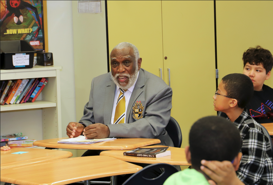 Alpha Phi Alpha members speak to students in a classroom.