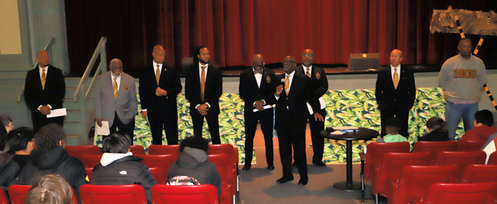 Alpha Phi Alpha members speak to students in the auditorium.