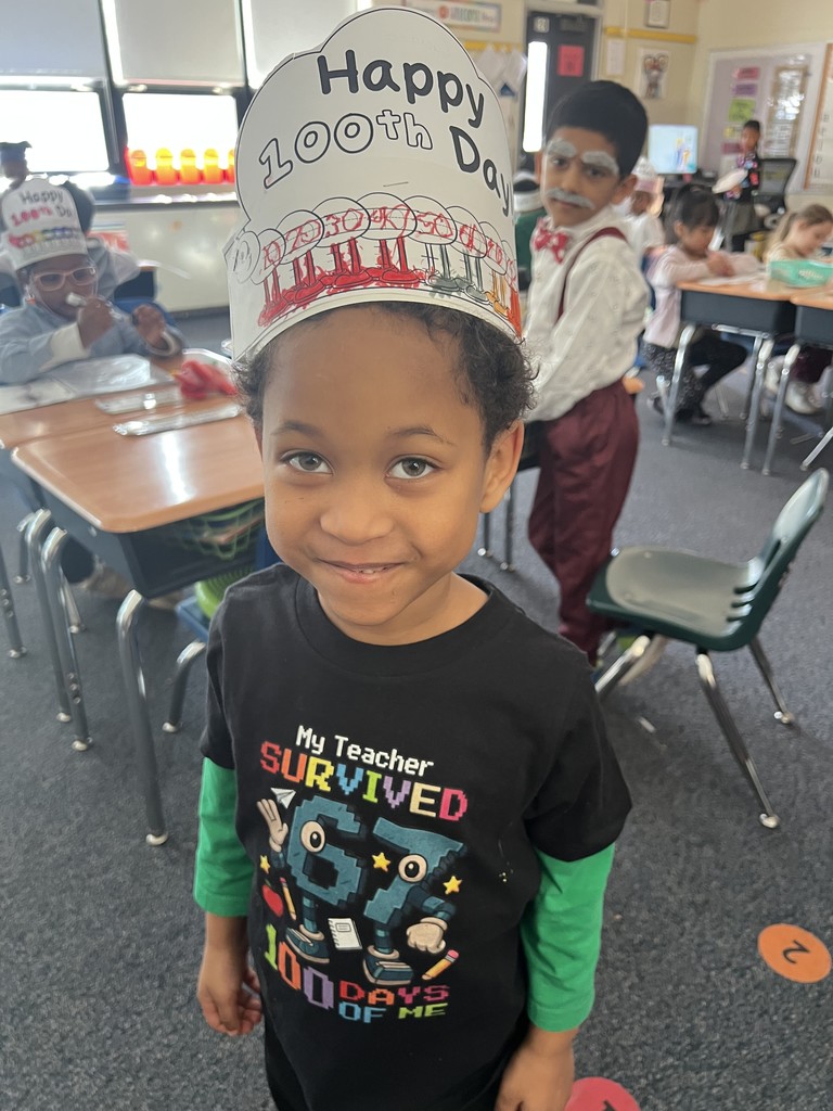 A student shows his 100th Day hat and shirt.