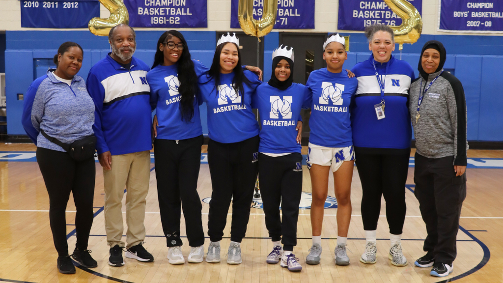 Girls basketball seniors pose for photo with coaches on the court.