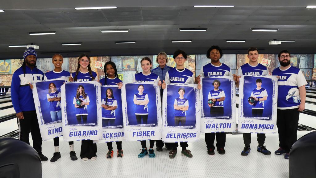 Bowling team seniors holding their senior posters, standing with coaches in front of bowling lane.