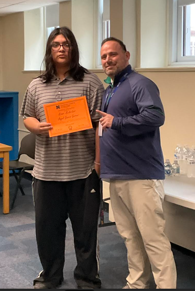 A student is posing with the principal in a classroom after receiving an award. They have the award in their hand.