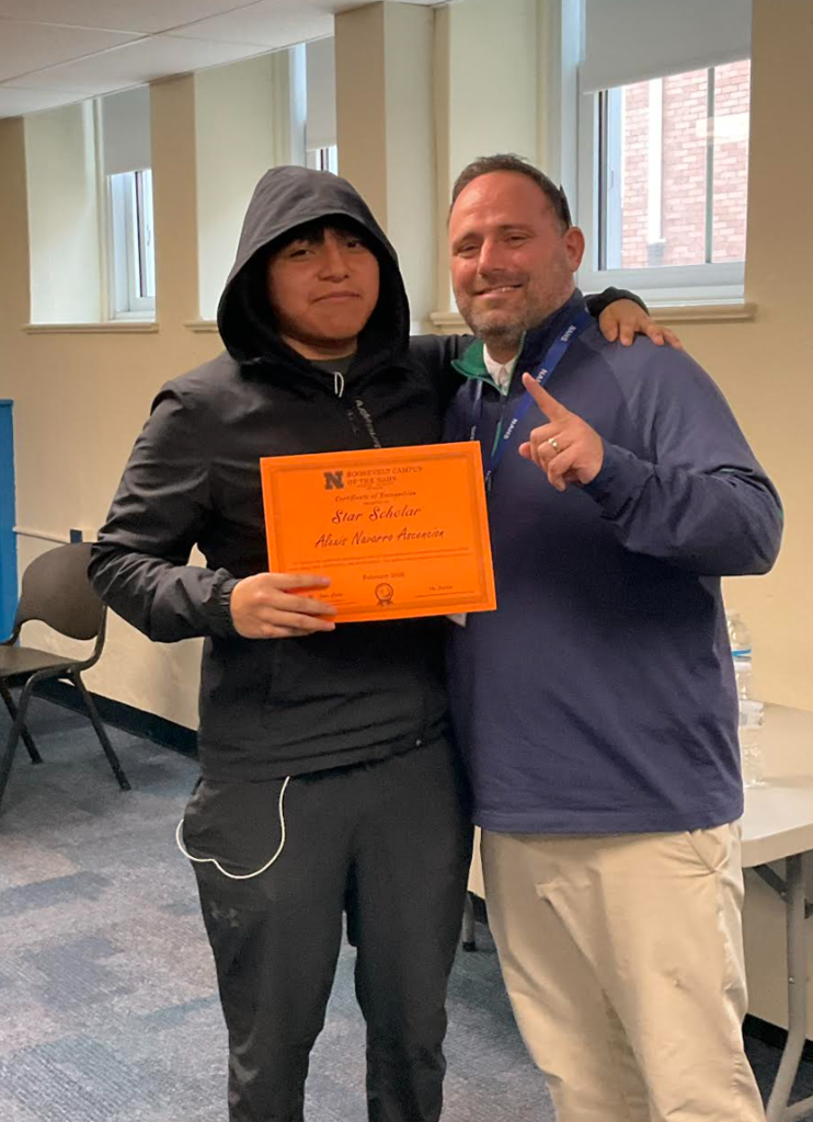 A student is posing with the principal in a classroom after receiving an award. They have the award in their hand.