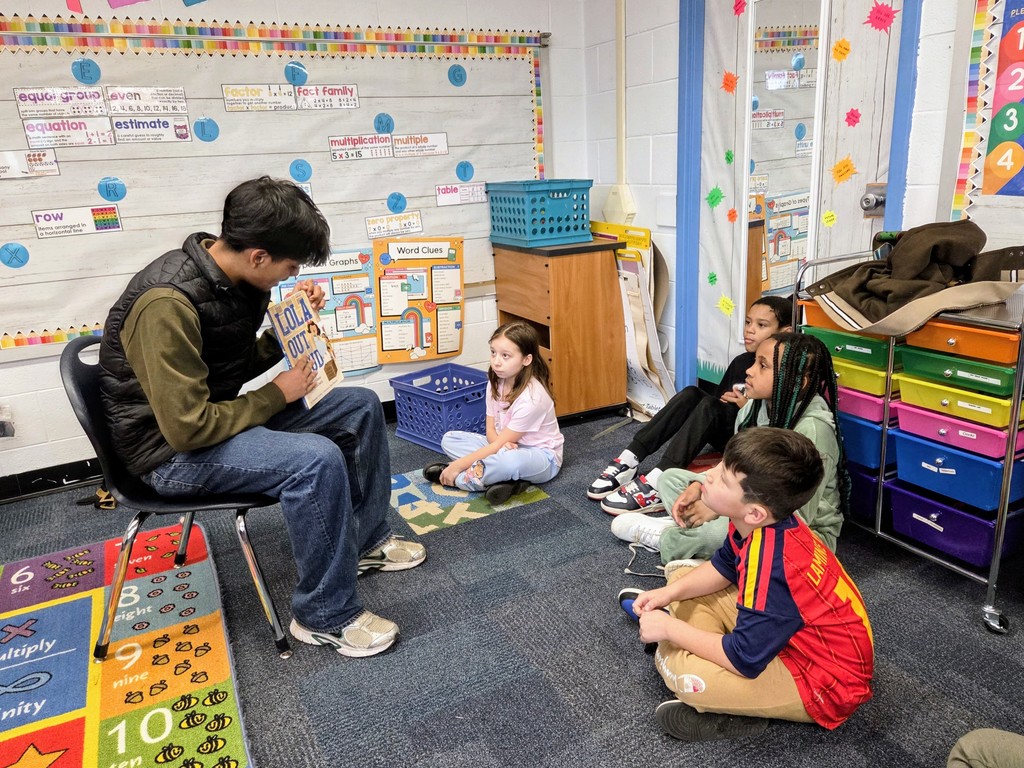 A highschool student reading to a small group of third graders