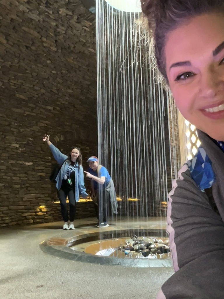 Three teachers are standing in front of a waterfall