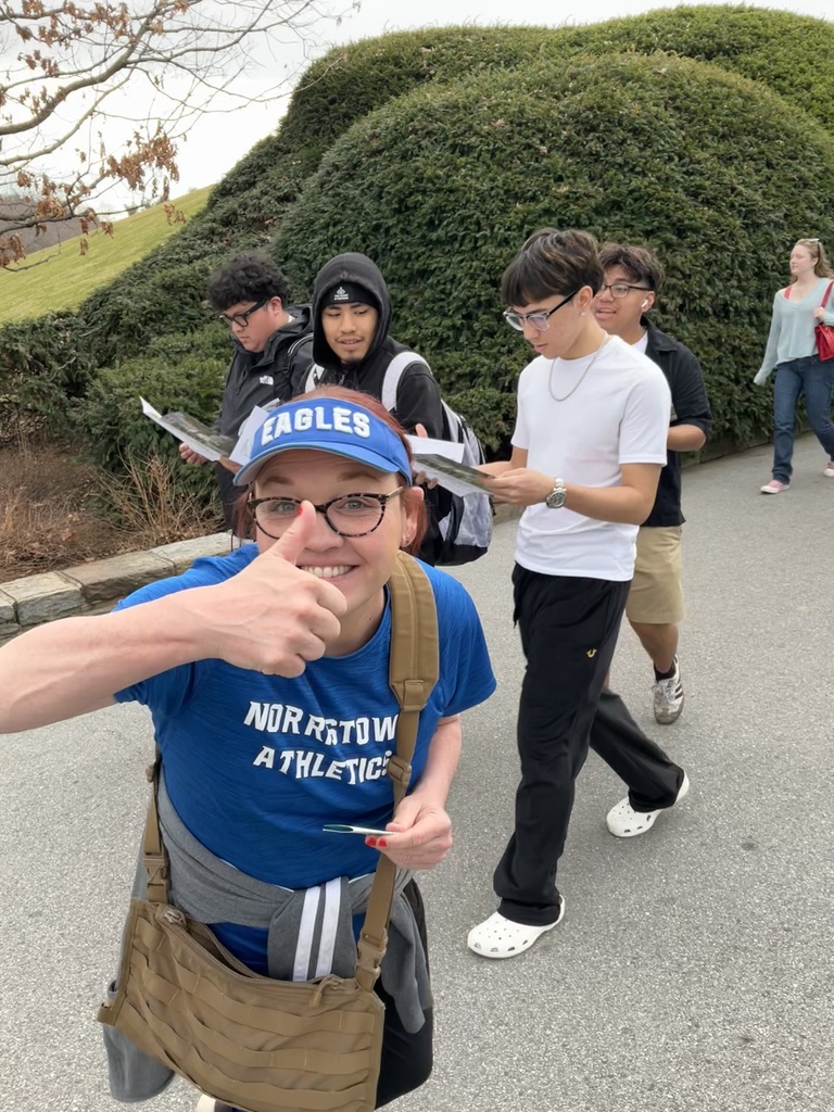 The counselor is giving a thumbs up with students behind her.