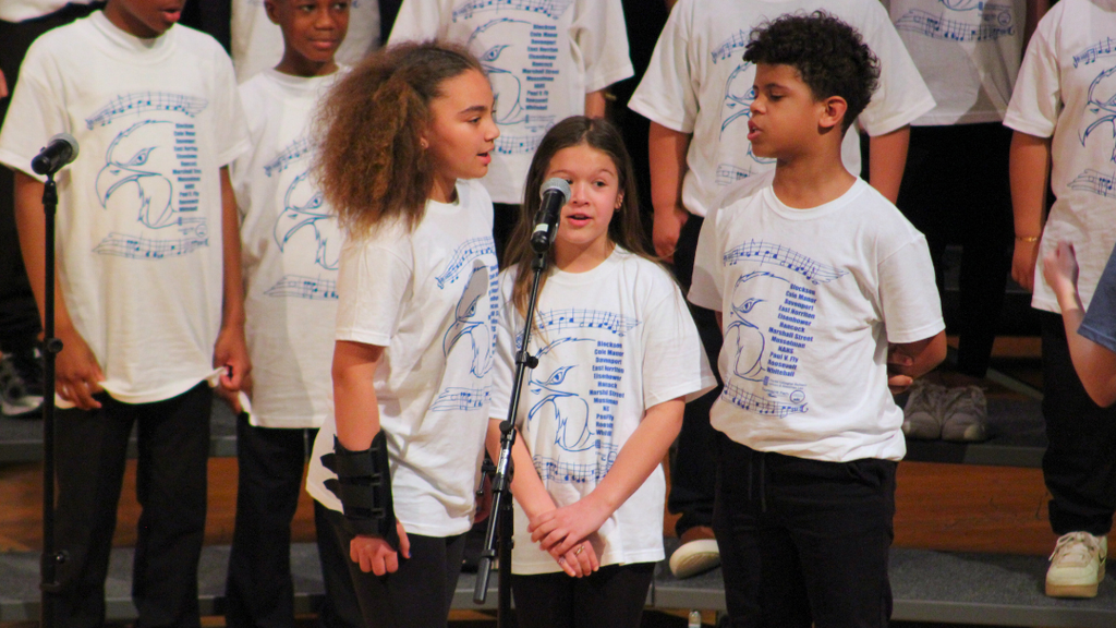 Three elementary students sining into a microphone on stage. 