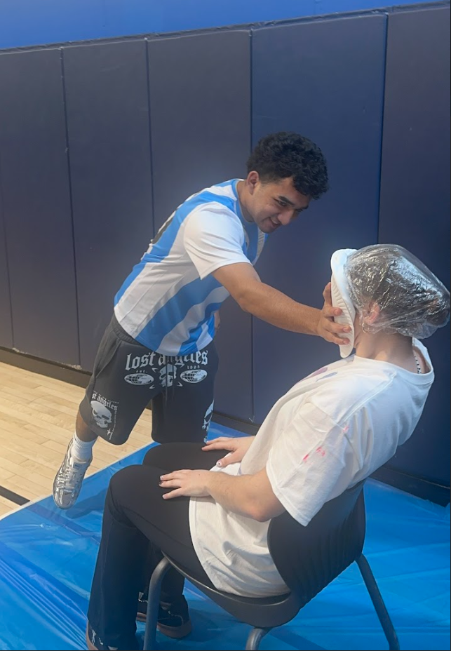 A student is throwing a pie in another person's face