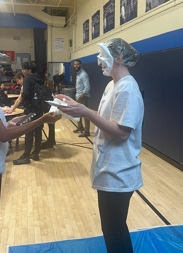 A city Year coach has a pie in her face and people in the background are laughing