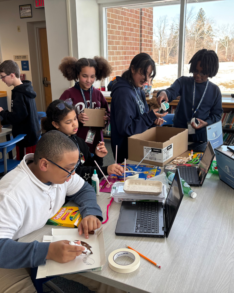 Group of 5 studnets working on their Dream It, Design It project with cardboard, markers, and their Chromebooks.