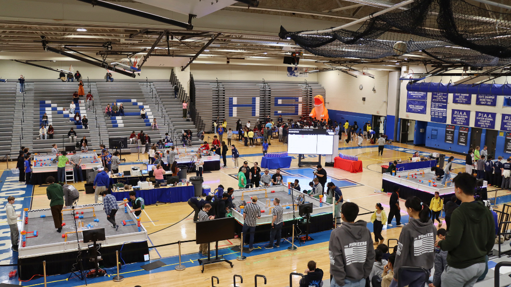 NAHS gymnasium hosting the robotics competition with multiple arenas, and people gathered around them.