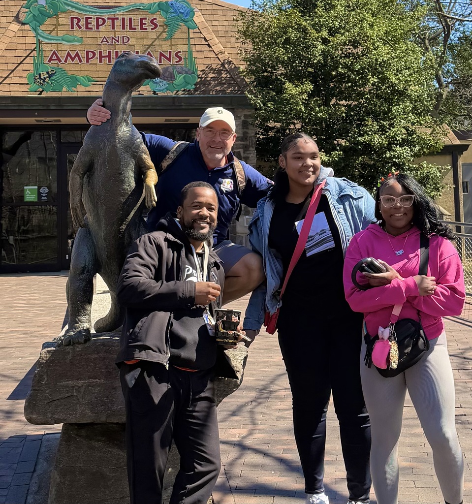 Philadelphia The Two teachers and two students are posing together for a picture with a reptile statue at the Philadelphia zoo.