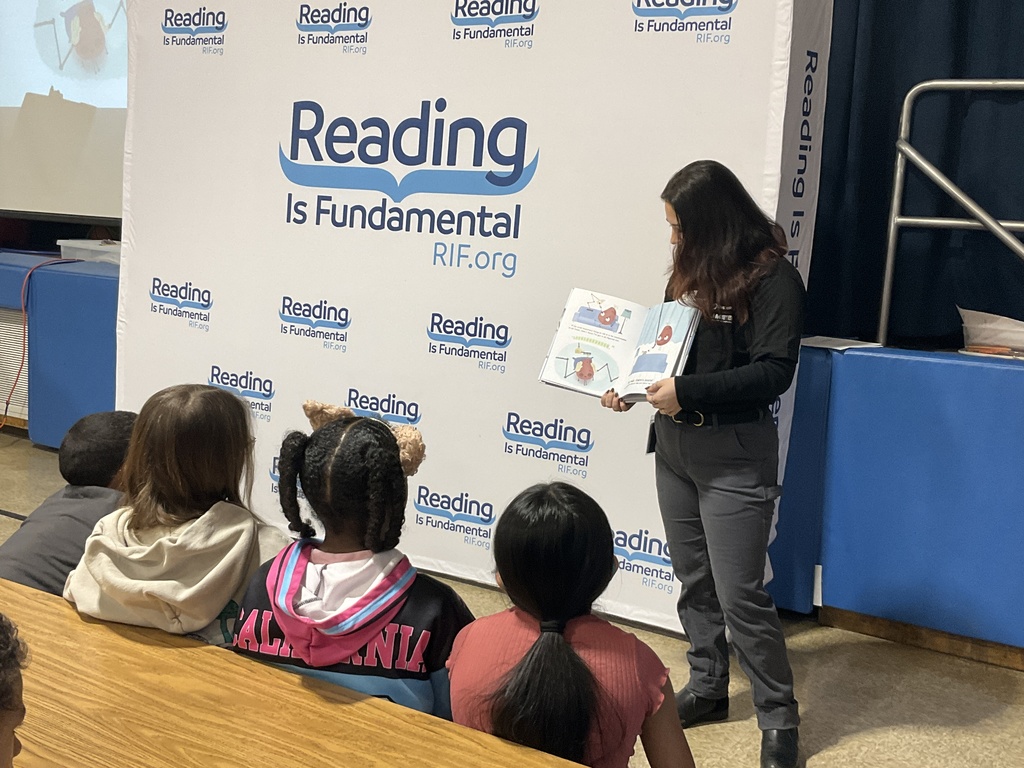 A volunteer holding up a book for students to see while listening to the read aloud