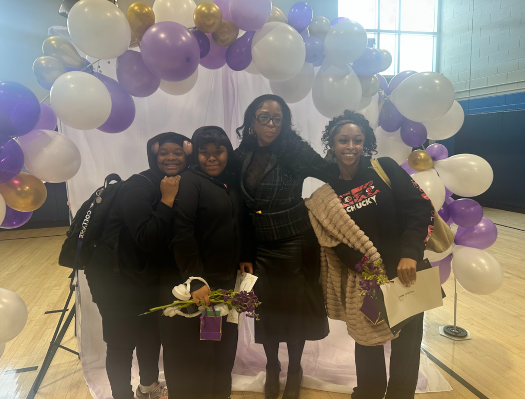 Students with a presenter are together under a balloon arch
