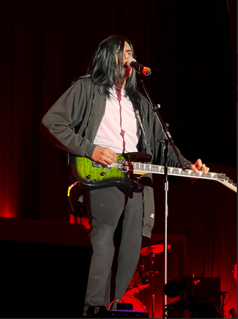 A student is on stage singing and playing his guitar