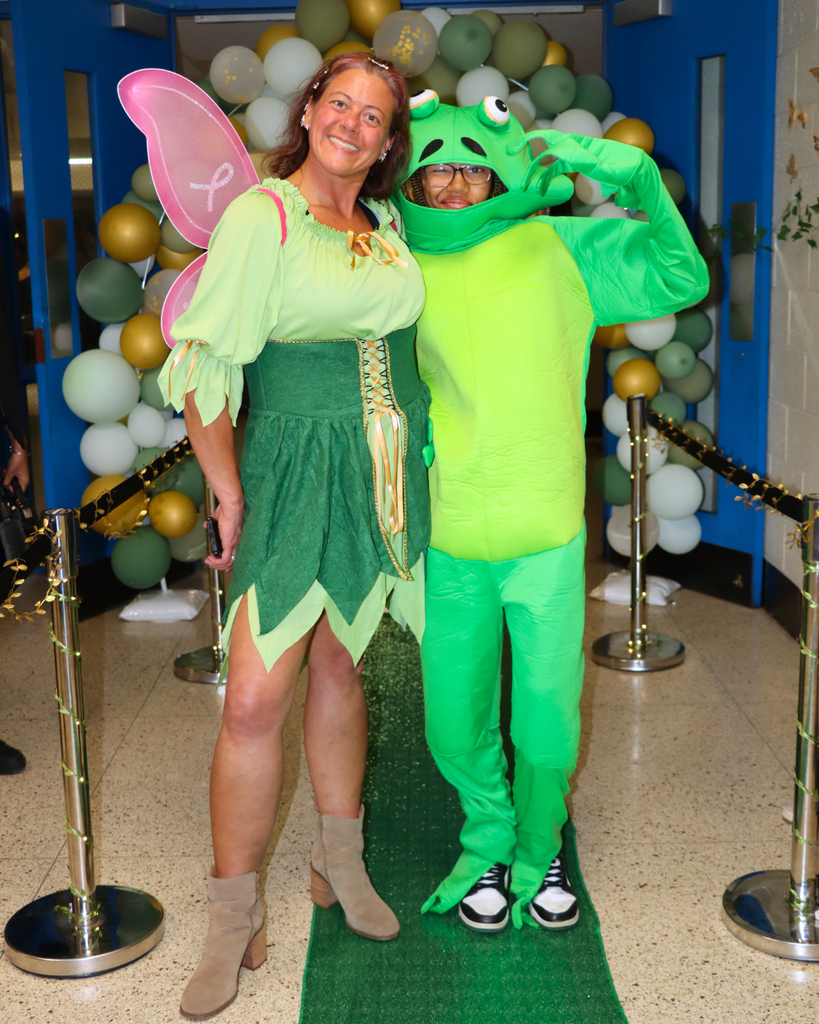 Teacher dressed as a princess and a student in a frog costume pose for photo in front of prom entrance. 