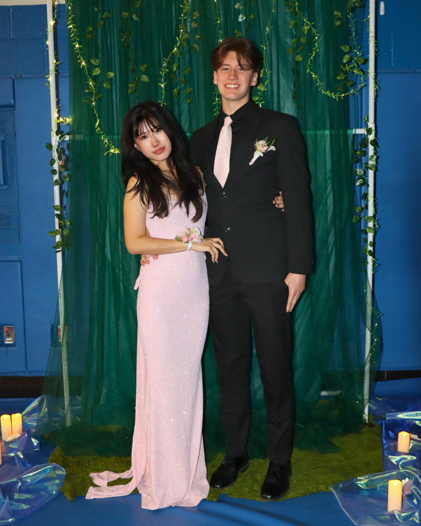 Two students at the junior prom posing for photo in front of green backdrop decorated with vines.