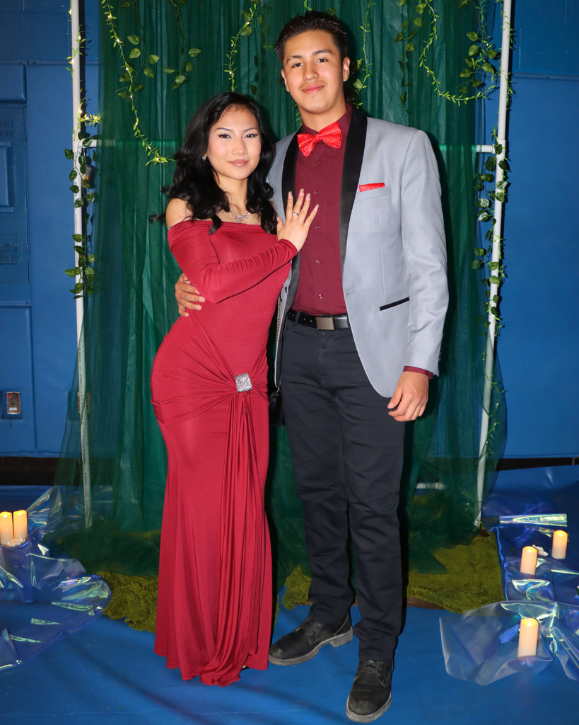Two students at the junior prom posing for photo in front of green backdrop decorated with vines.