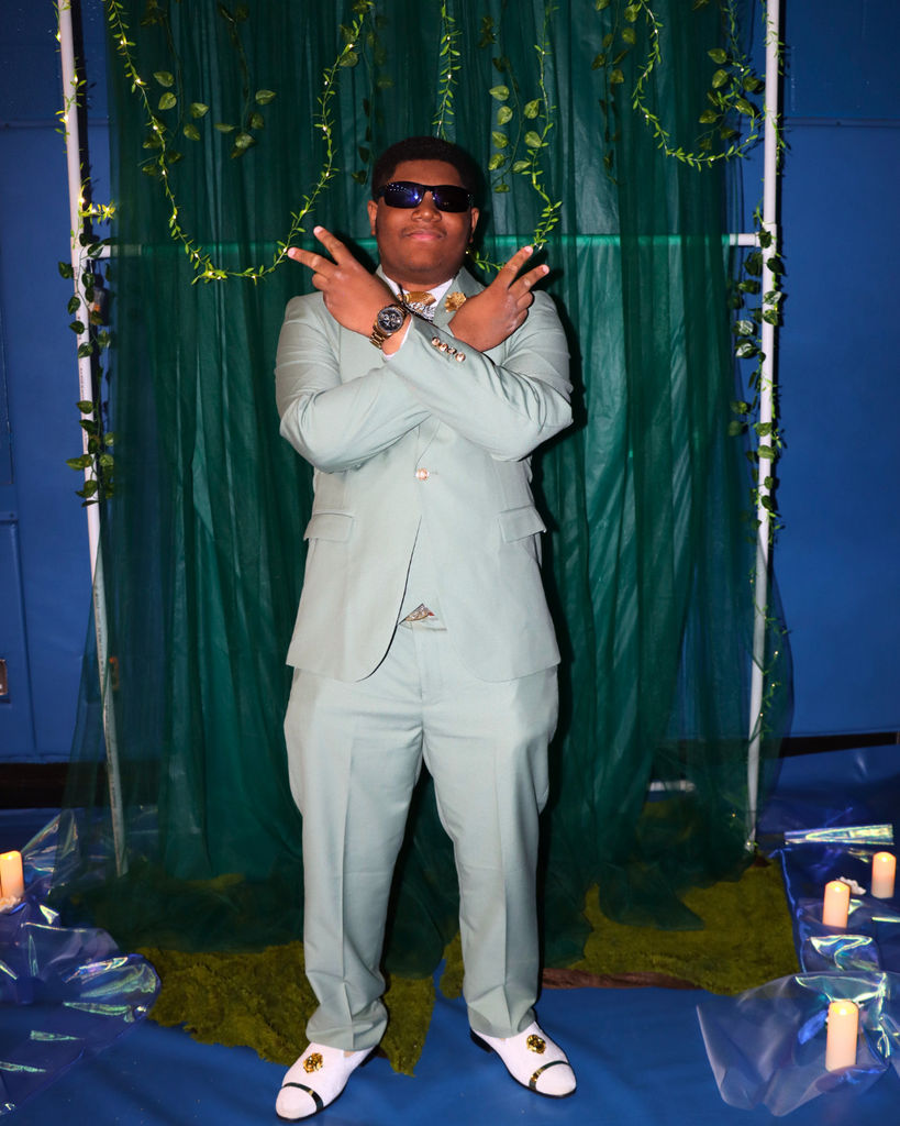 Student at the junior prom posing for photo in front of green backdrop decorated with vines.