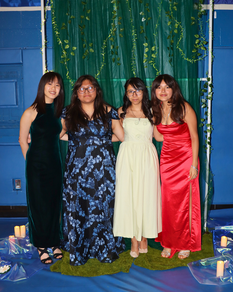 Four students at the junior prom posing for photo in front of green backdrop decorated with vines.