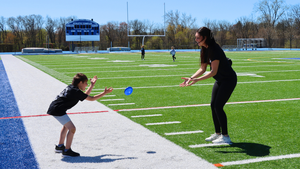 NASD student having a catch with a staff member on the turf field. 
