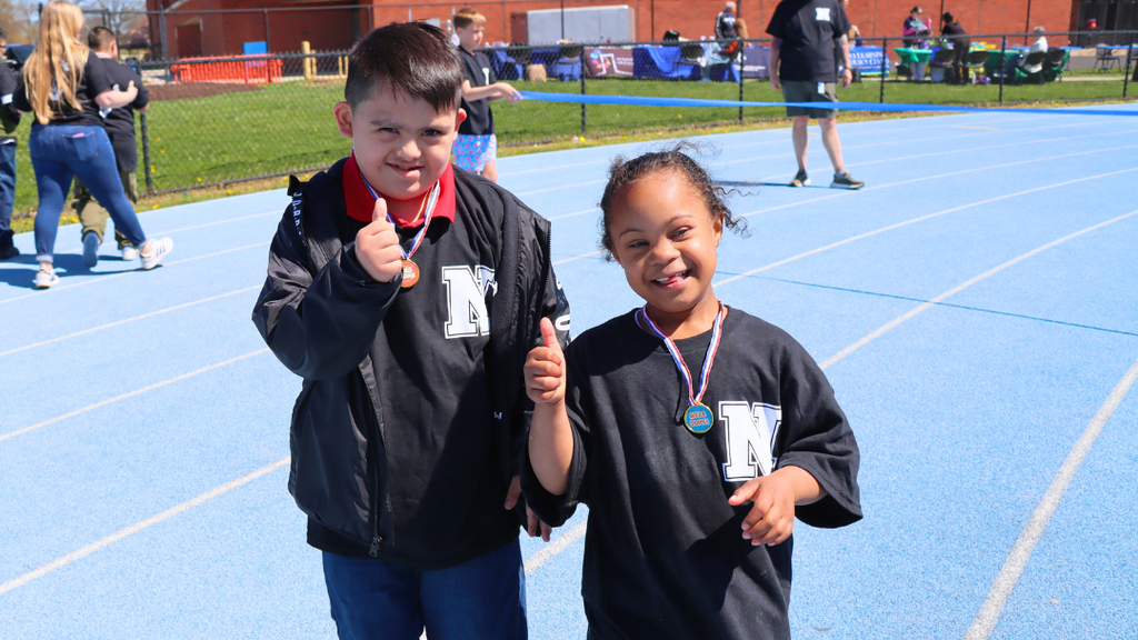 Two students giving a thumbs up wearing their participation medals on the track. 