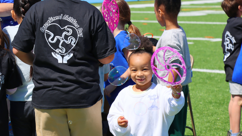 Young girl holding a bubble want with bubbles floating near her. 