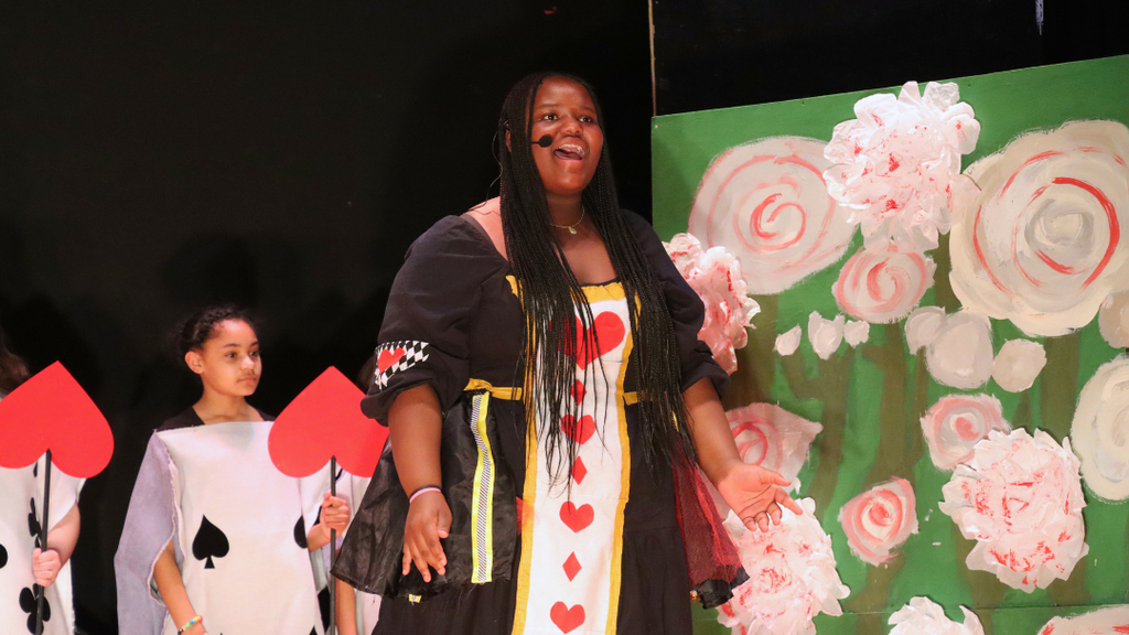Student performing on stage as the Queen of Hearts in Alice in Wonderland Jr.