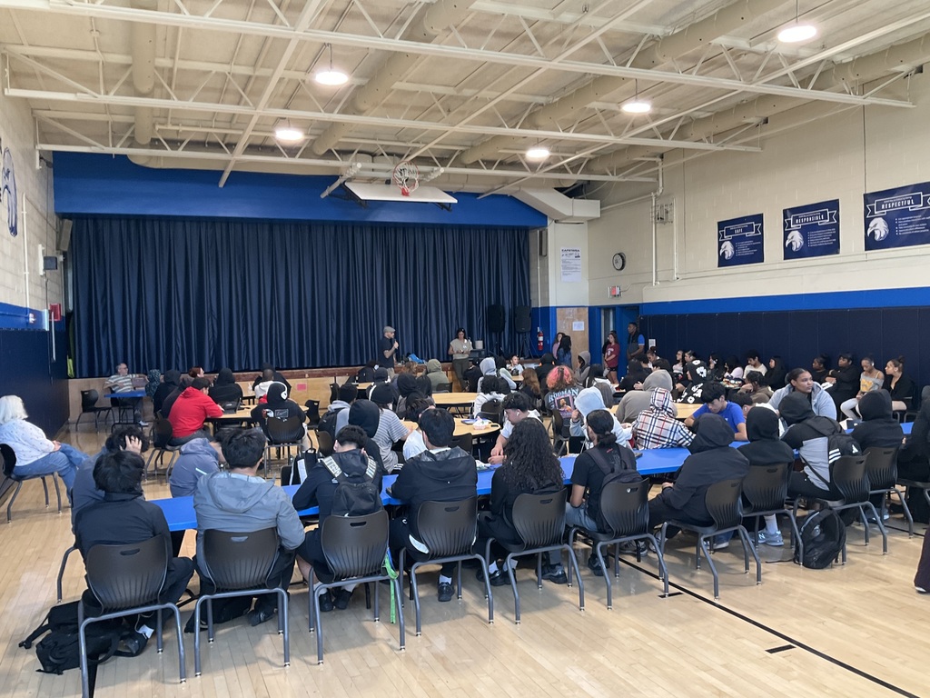 A group shot of the whole student body listening to the presenters in the gym