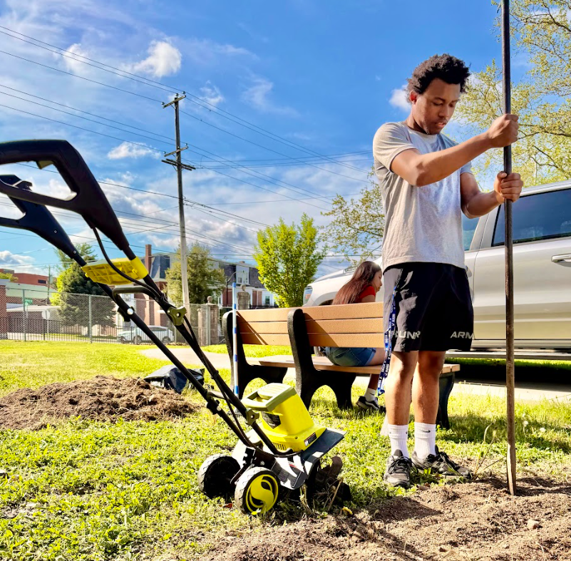 A student is holding a tool in the ground while working in the garden