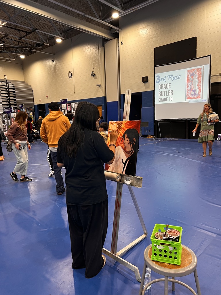 A student artist is painting on a canvas in the middle of the art show